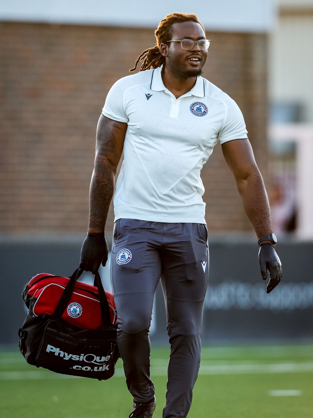 Jeremiah Adegoke, Chartered Physiotherapist, carrying a medical bag onto the pitch at Eastbourne Borough FC